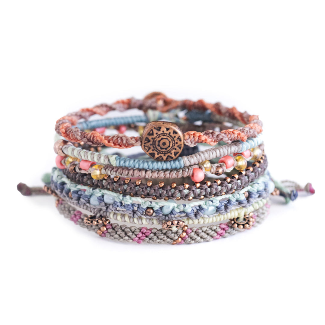 Colorful handmade woven bracelets with various beads and a central decorative bronze charm.